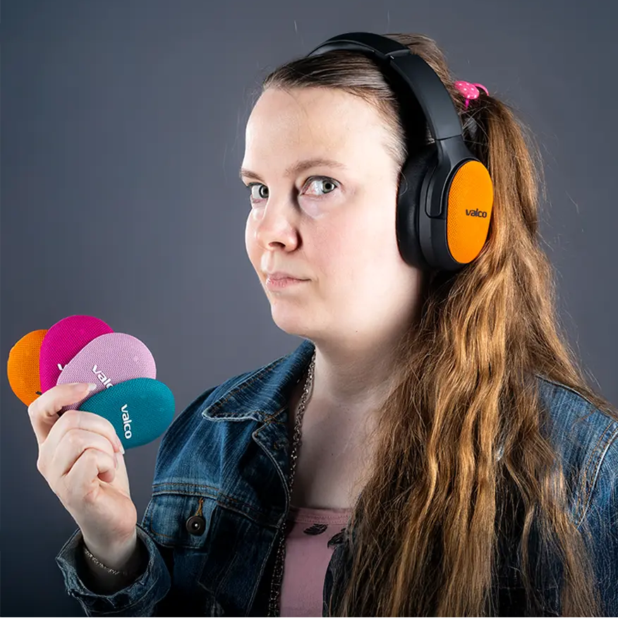Person wearing black Valco VMK25.2 headphones with an orange Skin cover and holding Skins in several colors