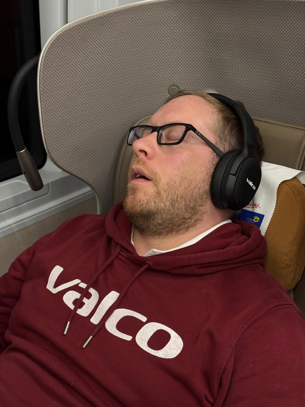 Mies nukkuu junan penkillä Valco-vastamelukuulokkeet päässä